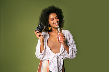 Pretty african woman with stislish hairstyle posing in studio, drinking lemonade from straw. Summer style. Green background. Bright make up.