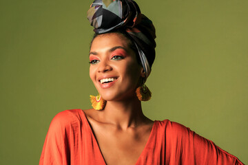 Laughing black  woman with  colorful turban in studio. Beautiful female model with vibrant makeup against  green background.