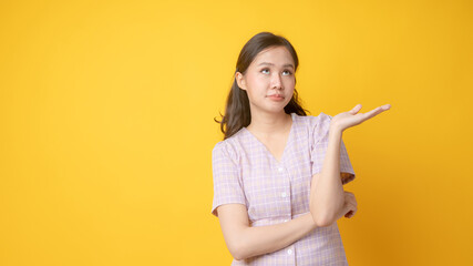 Portrait of Asian Thai woman poss as don't care and no interesting any thing with empty her left hand can put product isolated on yellow studio background.