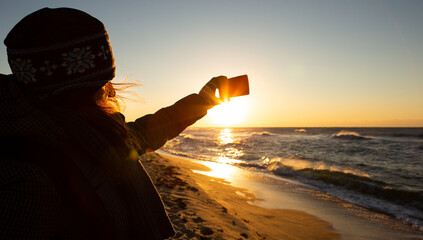 Woman traveler photographs the sea at sunrise on a smartphone camera.