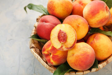 Fototapeta na wymiar Ripe peaches in a wicker basket on a stone gray table with a juicy peach slice with a stone pit.