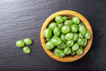 Fresh gooseberries in wooden bowl on black stone slate background.