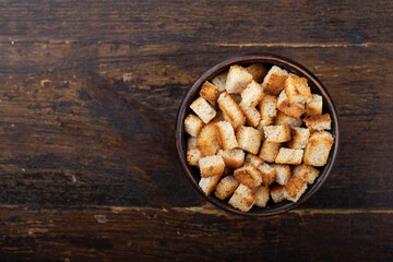 Crispy croutons in a bowl on a wooden background.