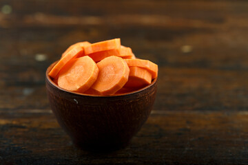 Sliced carrots in a bowl on a wooden background. Vegetable, ingredient and staple food.