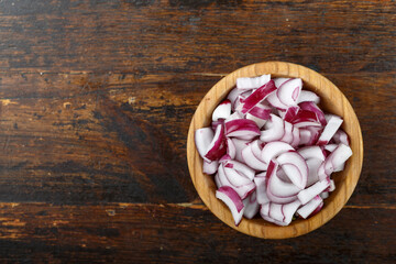 Obraz na płótnie Canvas Sliced raw red onion in a bowl on a wooden background. Vegetable, ingredient and staple food.