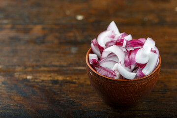Sliced raw red onion in a bowl on a wooden background. Vegetable, ingredient and staple food.