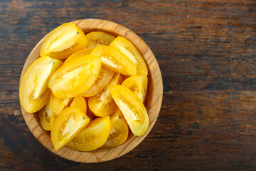 Sliced yellow tomato in a bowl on a wooden background. Vegetable, ingredient and staple food.