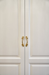 Classic white wardrobe with with ornamental golden handles close-up