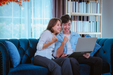 Portrait happy couple posing kiss to show  congratulation when they see special thing on notebook at sofa in living room.