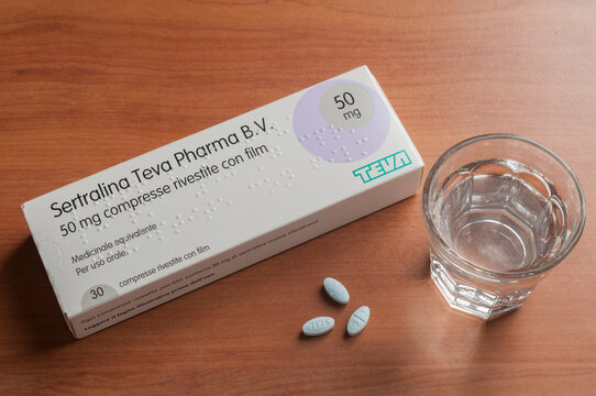 A box of sertraline tablets with a glass of water and some tablets on a wooden table