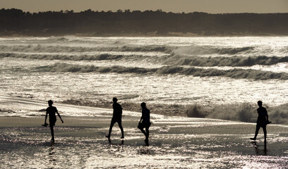 Fototapeta na wymiar Group of people walking along the shore of Valdoviño beach in Ferrol, Galicia, on sunny summer day at sunset in backlight