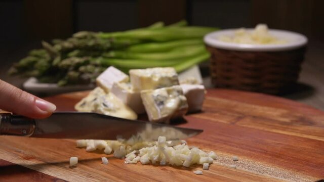 Close-up of the knife chopping garlic on the background of green asparagus spears and cheese