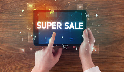Close-up of a hand holding tablet with SUPER SALE inscription, online shopping concept