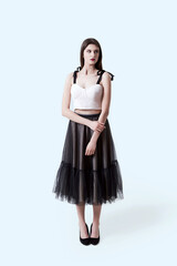 Young beautiful brunette girl in dark box pleated midi skirt posing in studio. Woman standing. Light grey background.