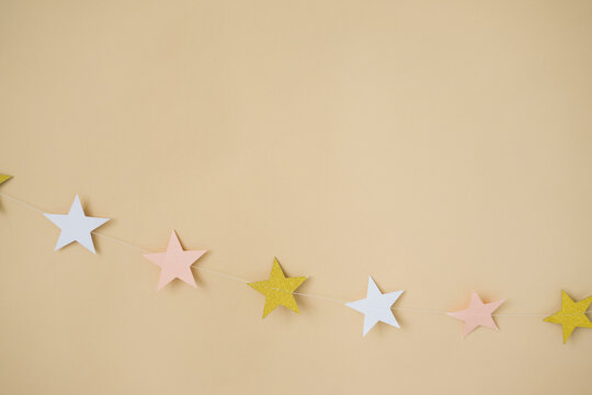 Garland Of Pink And Gold Paper Stars On A Beige Background. Decor For A Children's Party.