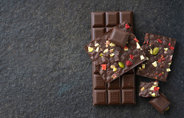 Black chocolate tile on a wooden board. Chocolate with slices of strawberries and pistachios on a black background