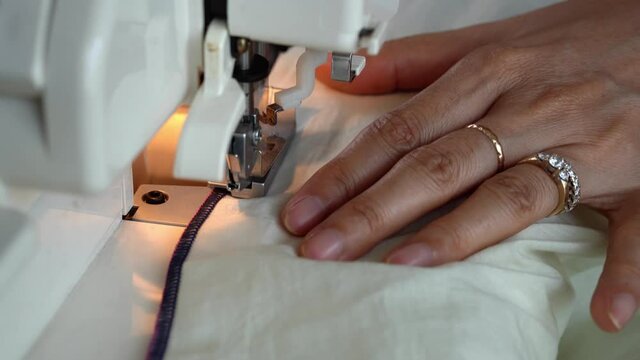 Overlock sewing machine closeup. Asian Seamstress hands.