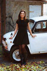 Fototapeta na wymiar young woman in a black dress in city with retro automobile