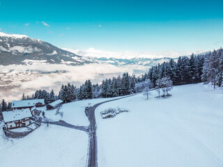 Fototapeta na wymiar Aerial view of snowy cloudy mountains, forest with a road, small chalet house. Captured from above with a drone. Dolomites Alps- Italy