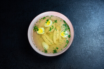 Soup with noodles, chicken, egg and dill on a dark background in a plate