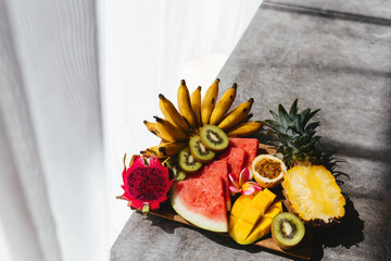 Tropical fruits assortment on a wooden plate. Stone background. Top view. Copy space.
