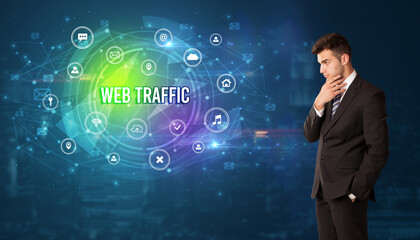 Businessman thinking in front of technology related icons and WEB TRAFFIC inscription, modern technology concept