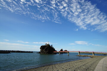 A beautiful blue sky behind a lighthouse and a red bridge in the beach, Japan