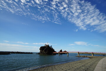 Fototapeta na wymiar A beautiful blue sky behind a lighthouse and a red bridge in the beach, Japan