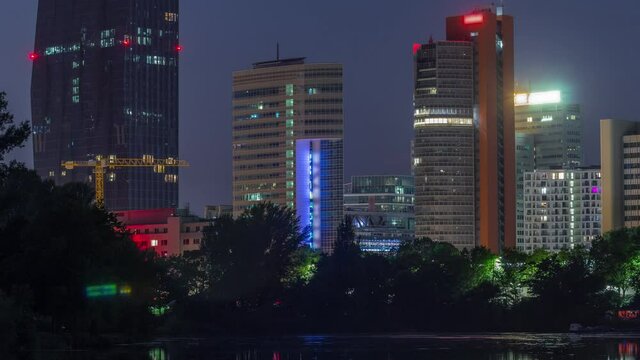 Vienna international center skyscrapers with Kaiserwasser lake reflection view day to night transition timelapse, Donaucity in capital of Austria. Colorful sky with clouds. Boats floating on a water