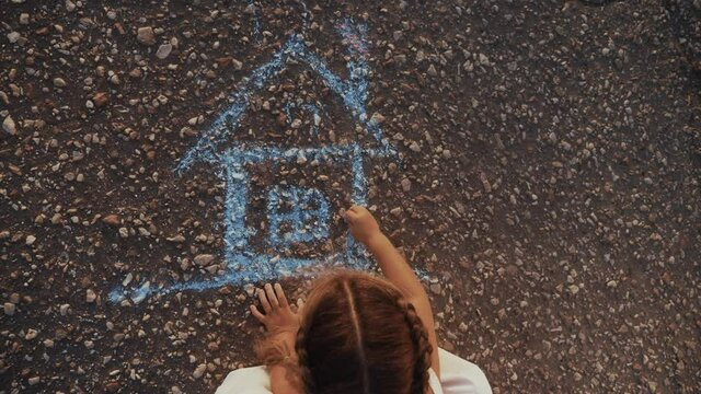 Child Kid Draw A House On The Asphalt With Chalk . Childhood Mortgage Dream Kid Concept. Little Girl Playing Draws With Chalk Big House. Concept Home Loan Mortgage For A Dream Residential Building