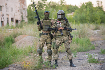 A professional airsoft player stands in a big helmet and a machine gun and with his partner