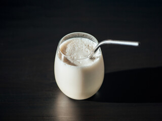 Protein milkshake in tumbler glass with metal straw over black background.