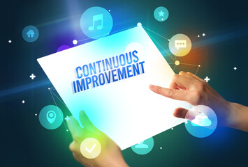 Holding futuristic tablet with CONTINUOUS IMPROVEMENT inscription, new technology concept