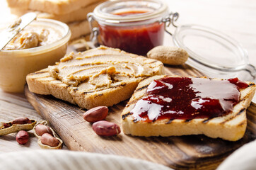 Low angle view at peanut butter and jam  sandwiches on cutting board with toasts aside. Healthy...