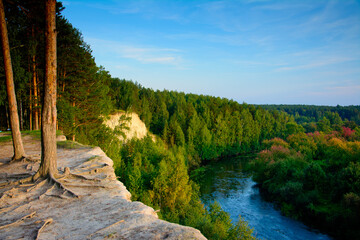 Clay mountain, cliff, nature of the Urals, sunset on the mountainside, river at the foot of the mountain, White mountain, view from the top, blue sky, trees with bare roots