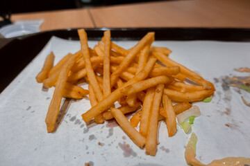 Close up of a bitten double cheeseburger on a tray with freshly cooked french fries inside a fast food restaurant in shopping mall