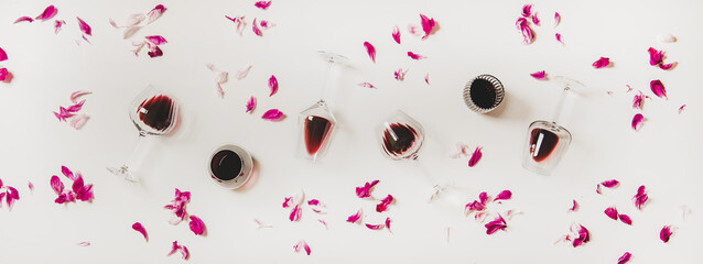 Red wine in glasses. Flat-lay of wine glasses with red wine and pink flowers petals over white...