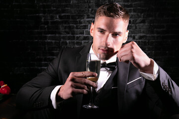 Portrait of handsome stylish man wearing a tuxedo holding up glass of sparkling wine and looking at camera.