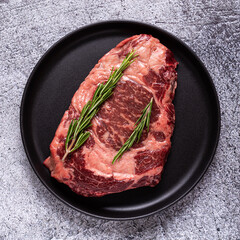 Fresh raw beef steak on black plate.