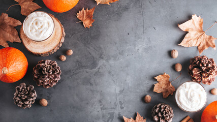 Autumn border with natural pine cones, pumpkins, dried leaves and pumpkin latte on dark grey stone top, top view, copy space. Fall, Thanksgiving background, cozy flat lay