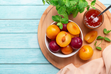 Yellow and red plums in a plate and jar of plum jam on blue wooden table flat lay, autumn fruit preserves concept, copy space