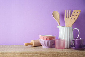 Kitchen utensils and dishware on wooden shelf. Kitchen interior purple background