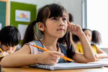 Portrait of an Asian child girl student thinking and solving the subject matter studied in the...