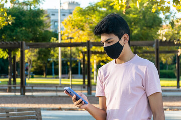 Obraz premium Young man wearing a medical mask using her phone at the park.