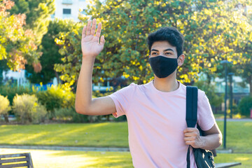 Naklejka premium A young man with a medical mask waving to someone in the park.