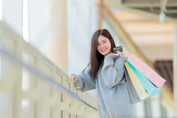 Beautiful asian woman teenager holding credit card and colorful shopping bags, looking at camera in big shopping mall. Copy space