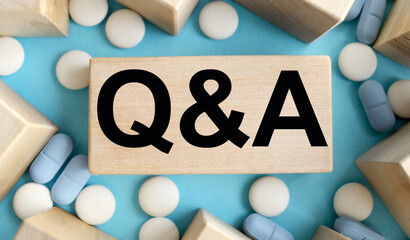 Q & A FAQ Questions and answers on wooden cube blocks on grey background with scattered blue pills from a white jar. Medical questions and answers concept