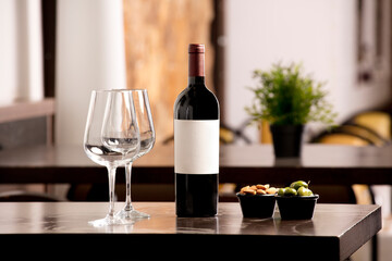 Wine bottle with white label for text with wine glasses and olives and almonds, on top of the...