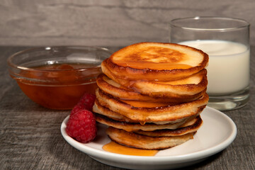 Several pancakes with apricot jam, raspberry and glass of milk on wood background