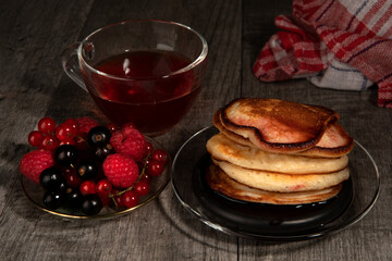 Several pancakes with different berries and tea on wood background